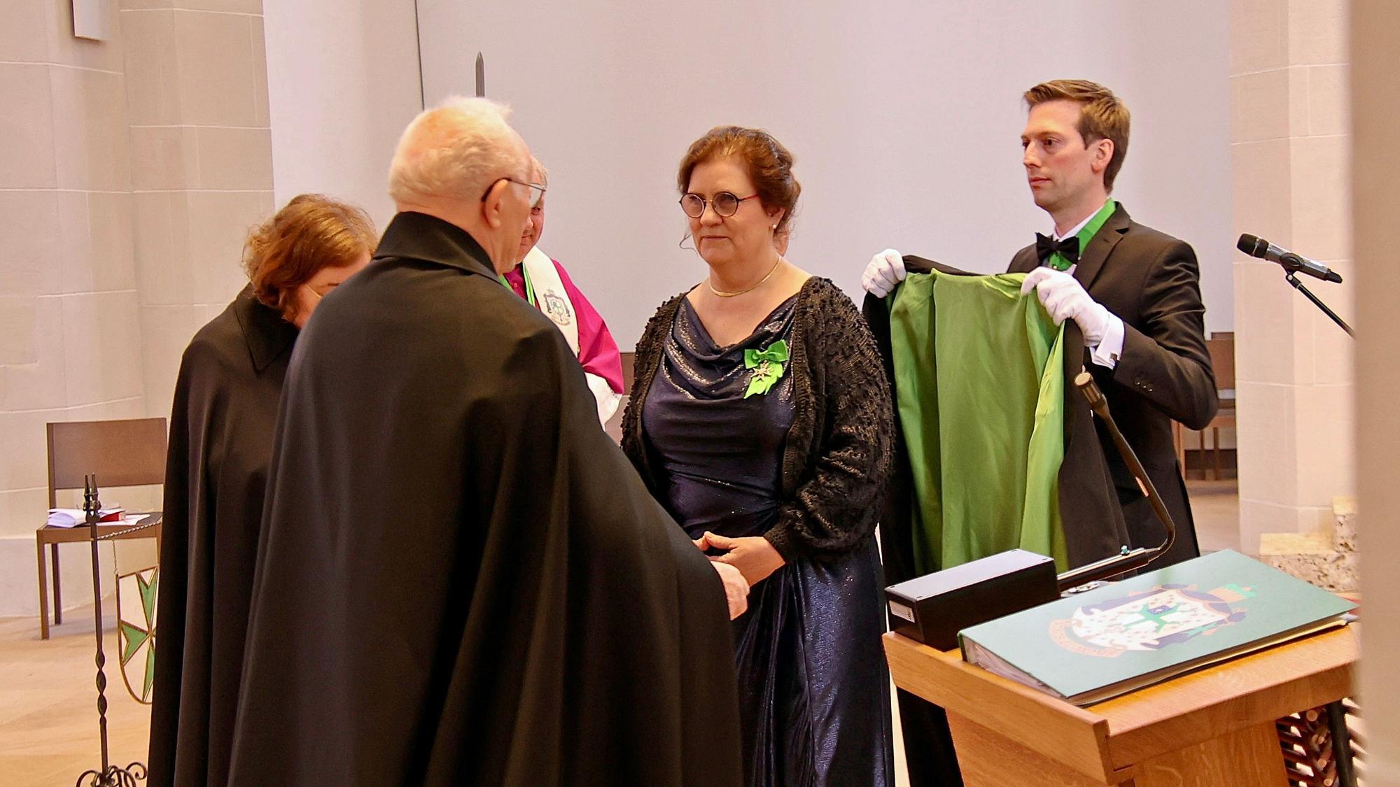 Inge Hartmann steht vor ihrem Vorgesetzten und kriegt einen grün-schwarzen Mantel umgelegt.