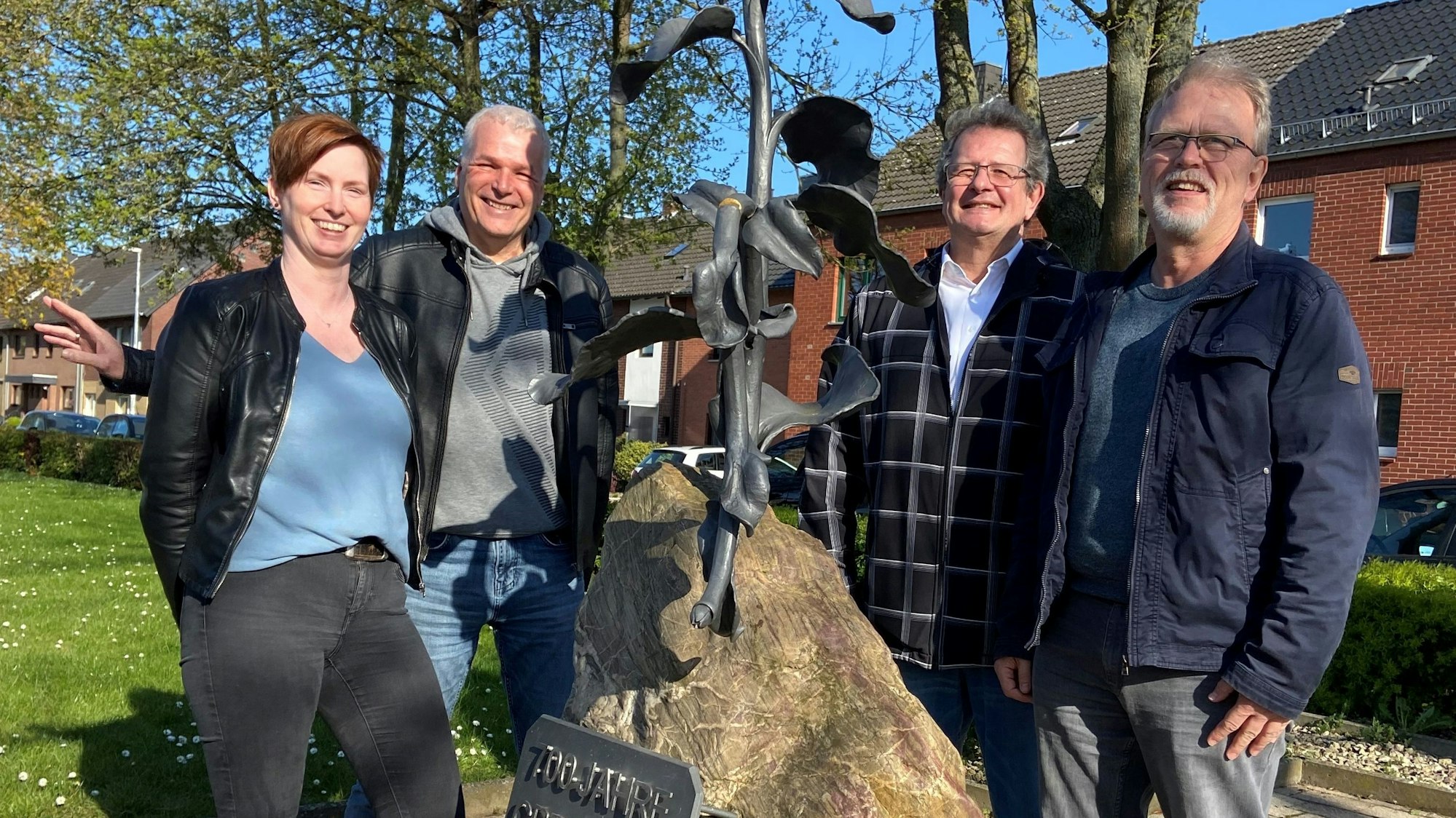Die Mitglieder des Kultur- und Heimtvereins Grefrath lachen in die Kamera und stehen vor einem Denkmal.