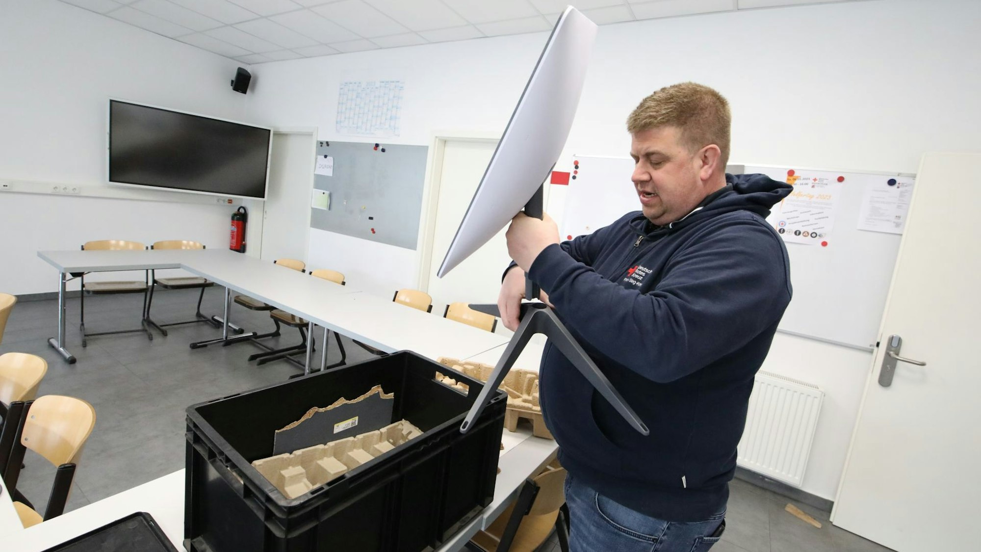 Ein Mann hält eine weiße Satellitenschüssel in der Hand und montiert sie an einen Ständer. Auf dem Tisch davor steht eine schwarze Kiste.