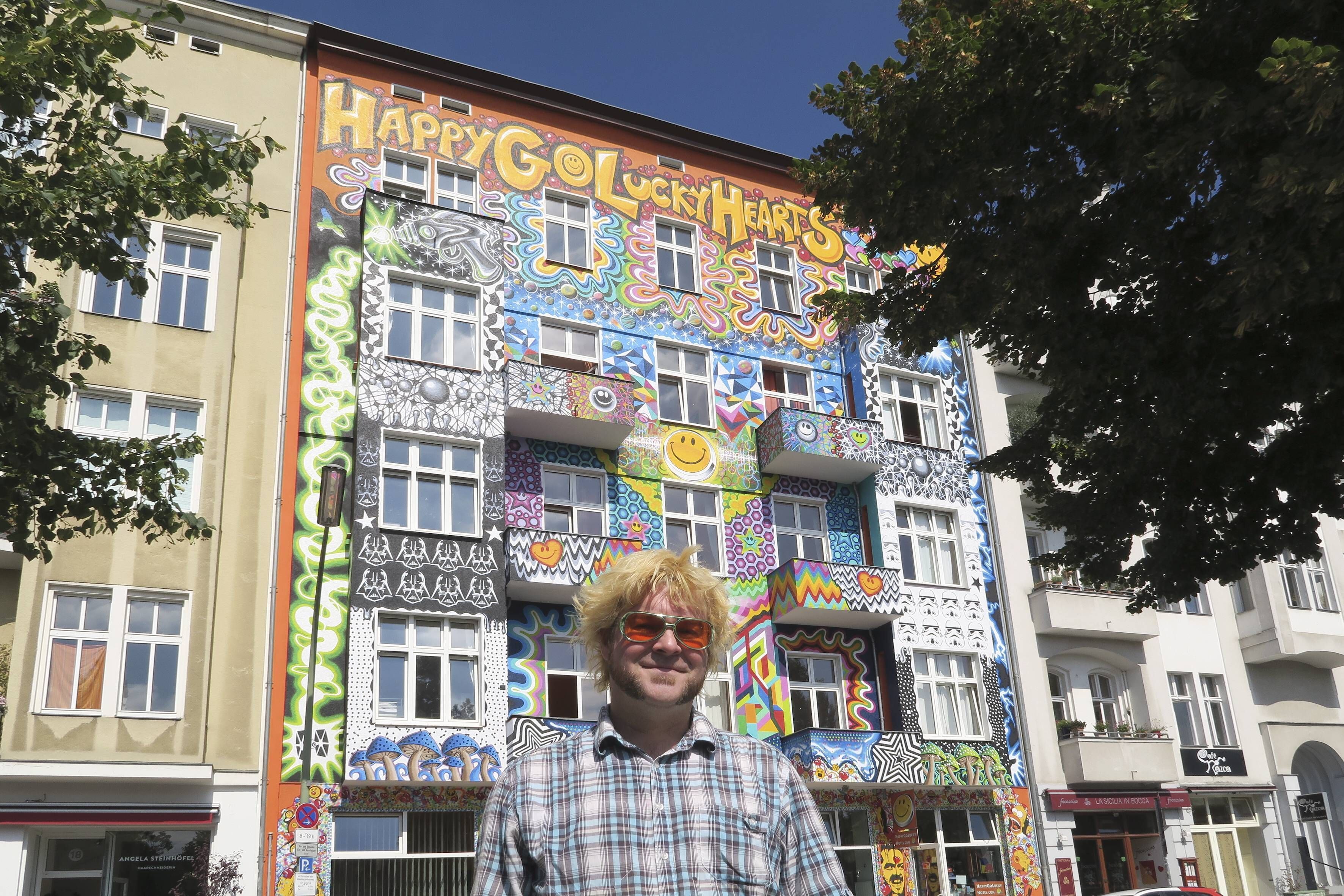 August 2018: Der irische Künstler Dom Browne steht vor seinem Wandgemälde am Berliner Hostel.
