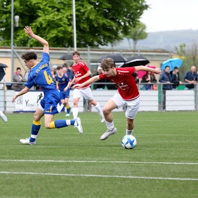 Ein Spieler der JSG Erft 01 im roten Trikot und weißer Hose lässt einen Spieler des 1. FC Düren II ganz in blau aussteigen.