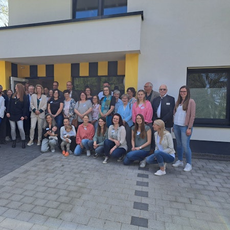 Vor dem Gebäude stehen Helfer und Helferinnen bei der Einweihung.