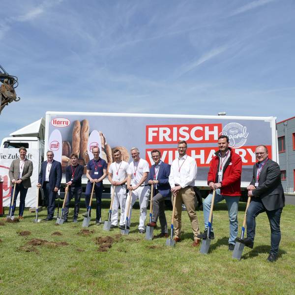 Wichtige Menschen von Harry Brot beim Spatenstich, im Hintergrund sieht man einen Bagger und einen LKW mit dem Firmen-Logo.