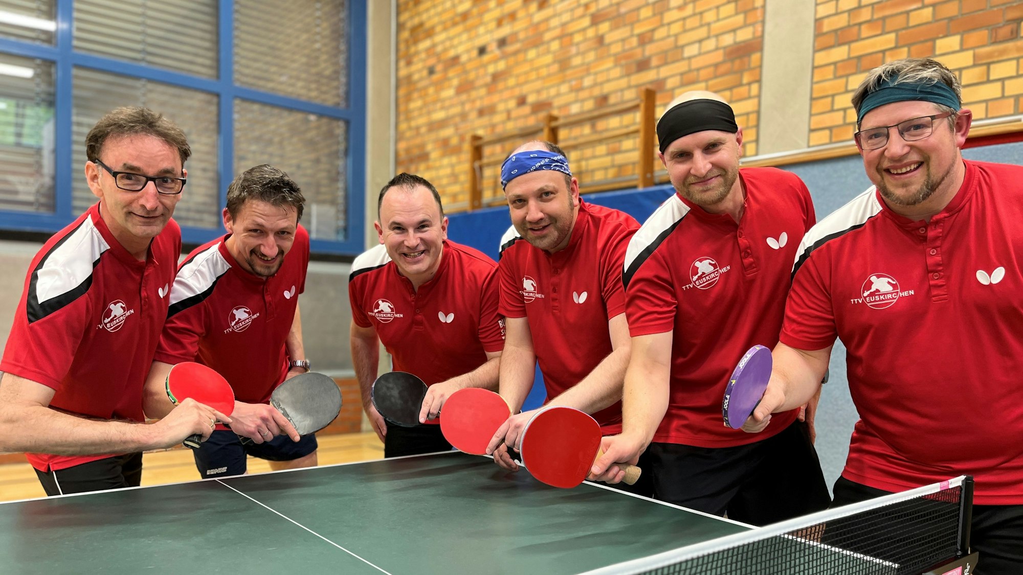 Sechs Tischtennisspieler posieren mit Schläger an einer Platte.