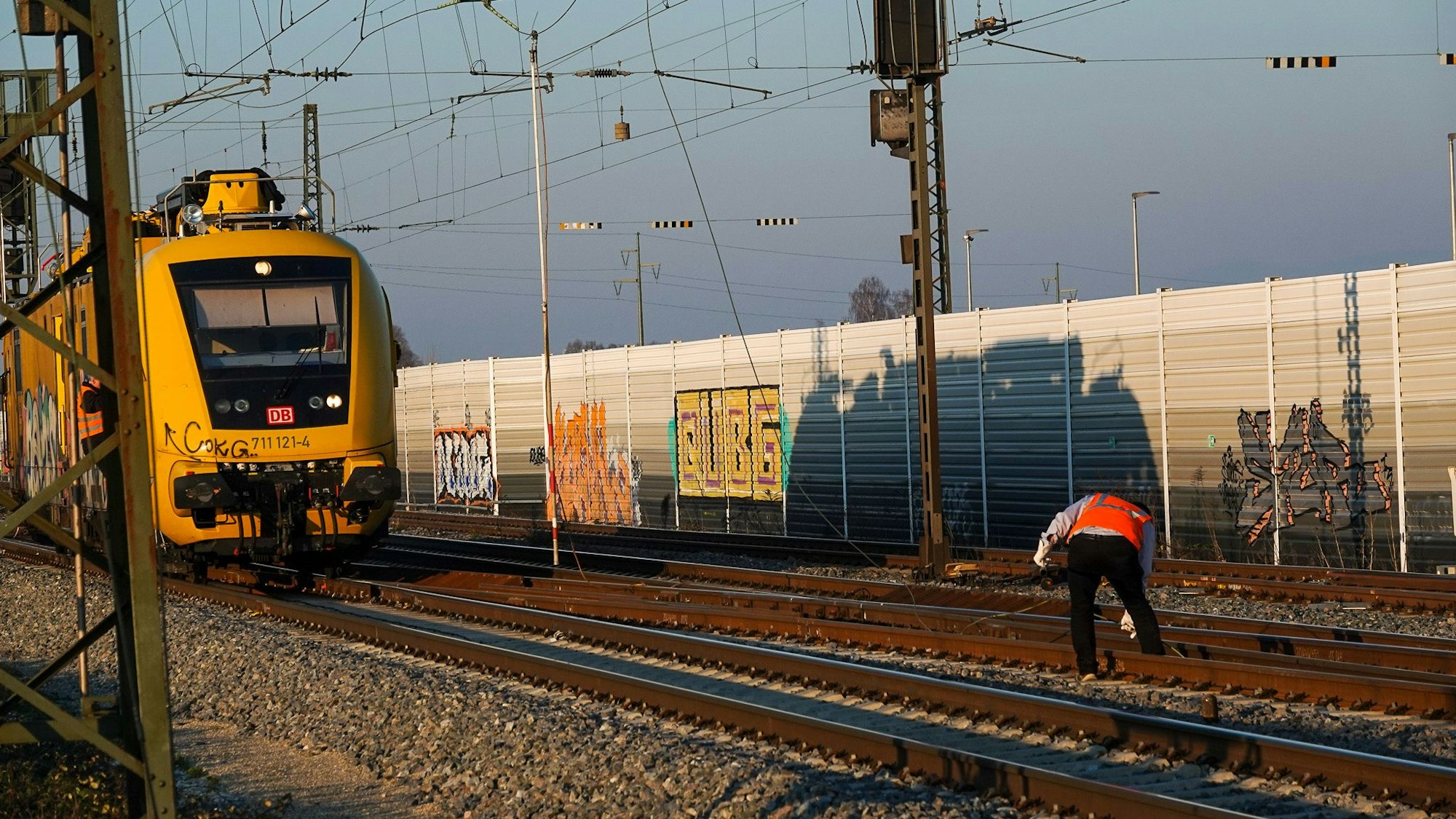 Ein Mitarbeiter der Bahn steht zwischen den Gleisen und greift nach einem Teil der Oberleitung.