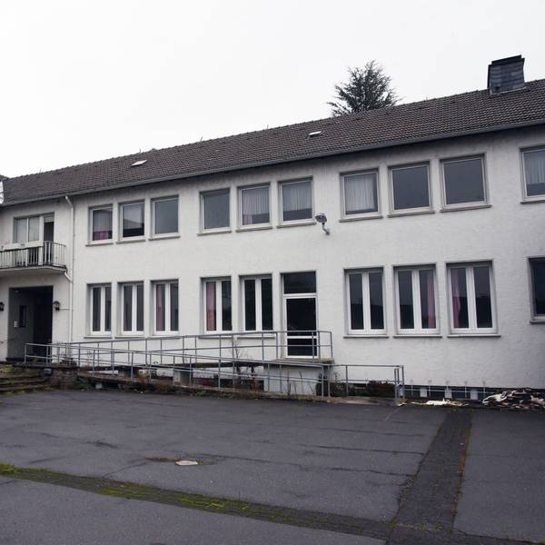 Ein weißes Gebäude mit dunklem Dach und einem asphaltierten Hof.