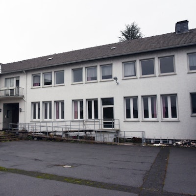 Ein weißes Gebäude mit dunklem Dach und einem asphaltierten Hof.