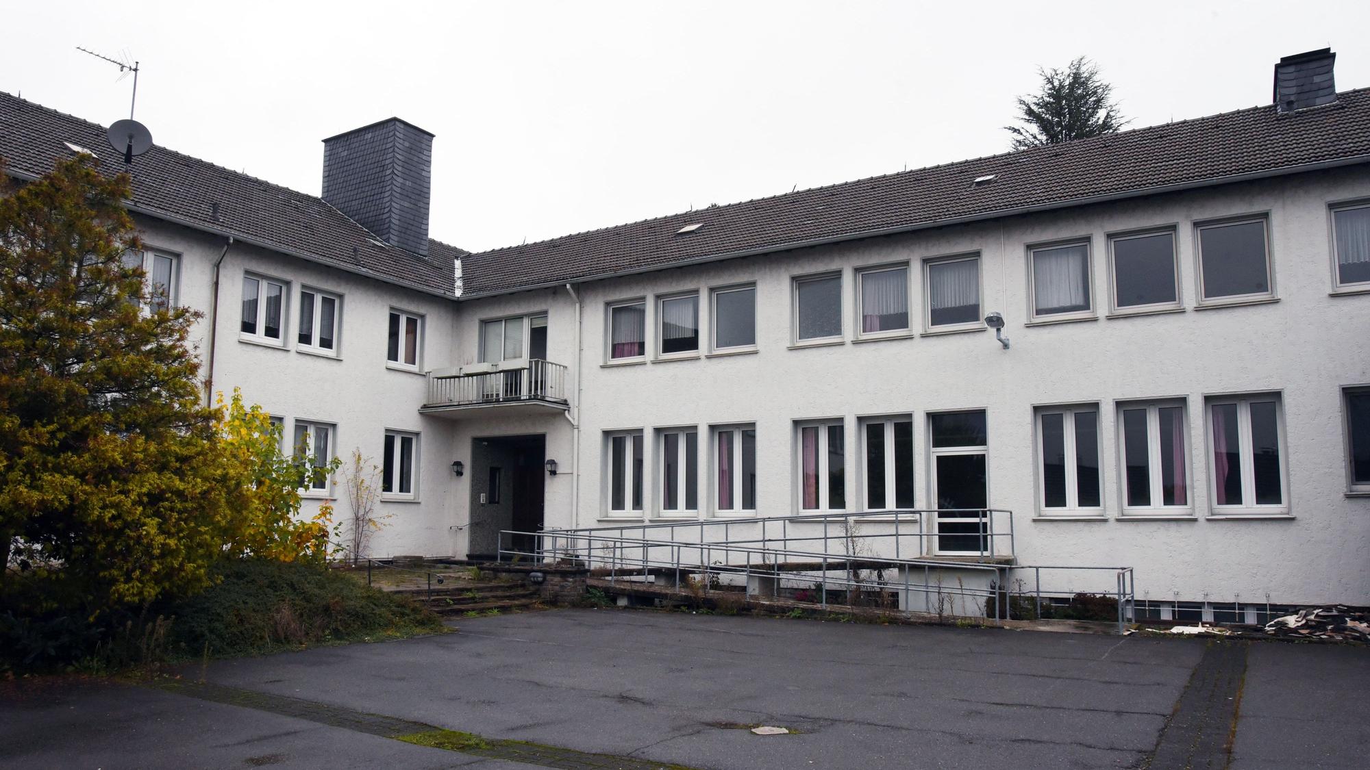Ein weißes Gebäude mit dunklem Dach und einem asphaltierten Hof.