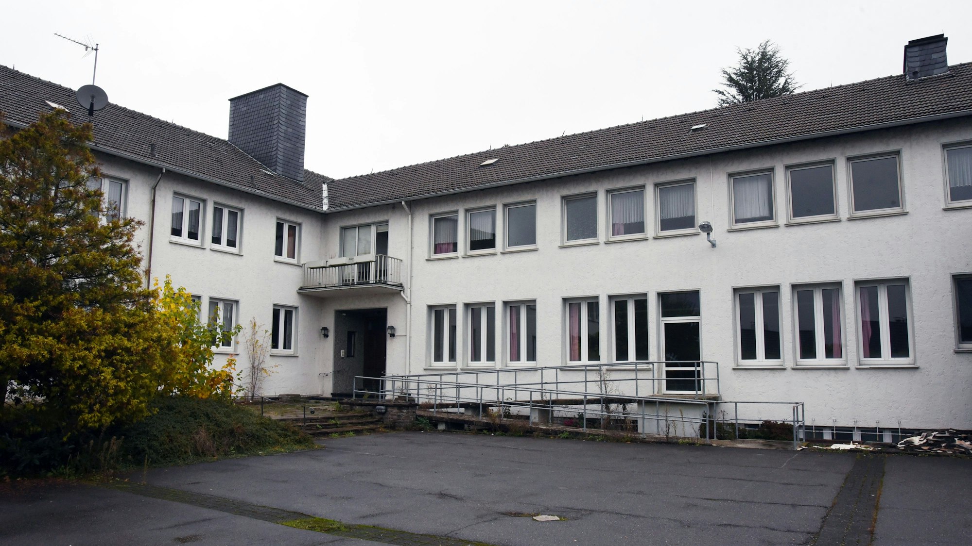 Ein weißes Gebäude mit dunklem Dach und einem asphaltierten Hof.