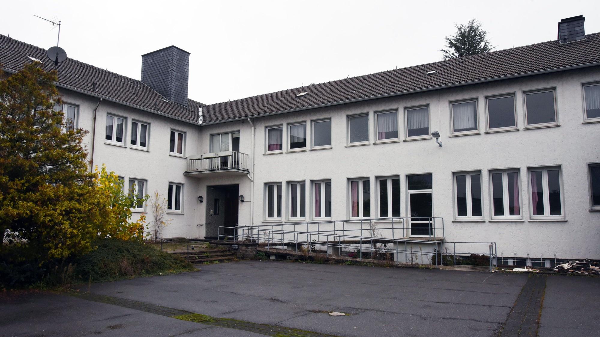 Ein weißes Gebäude mit dunklem Dach und einem asphaltierten Hof.