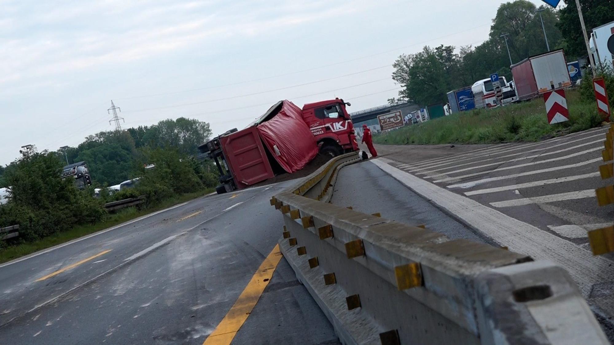 Auf der sonst leeren Fahrbahn liegt ein gekippter Auflieger, aus dem Erde herausgefallen ist.