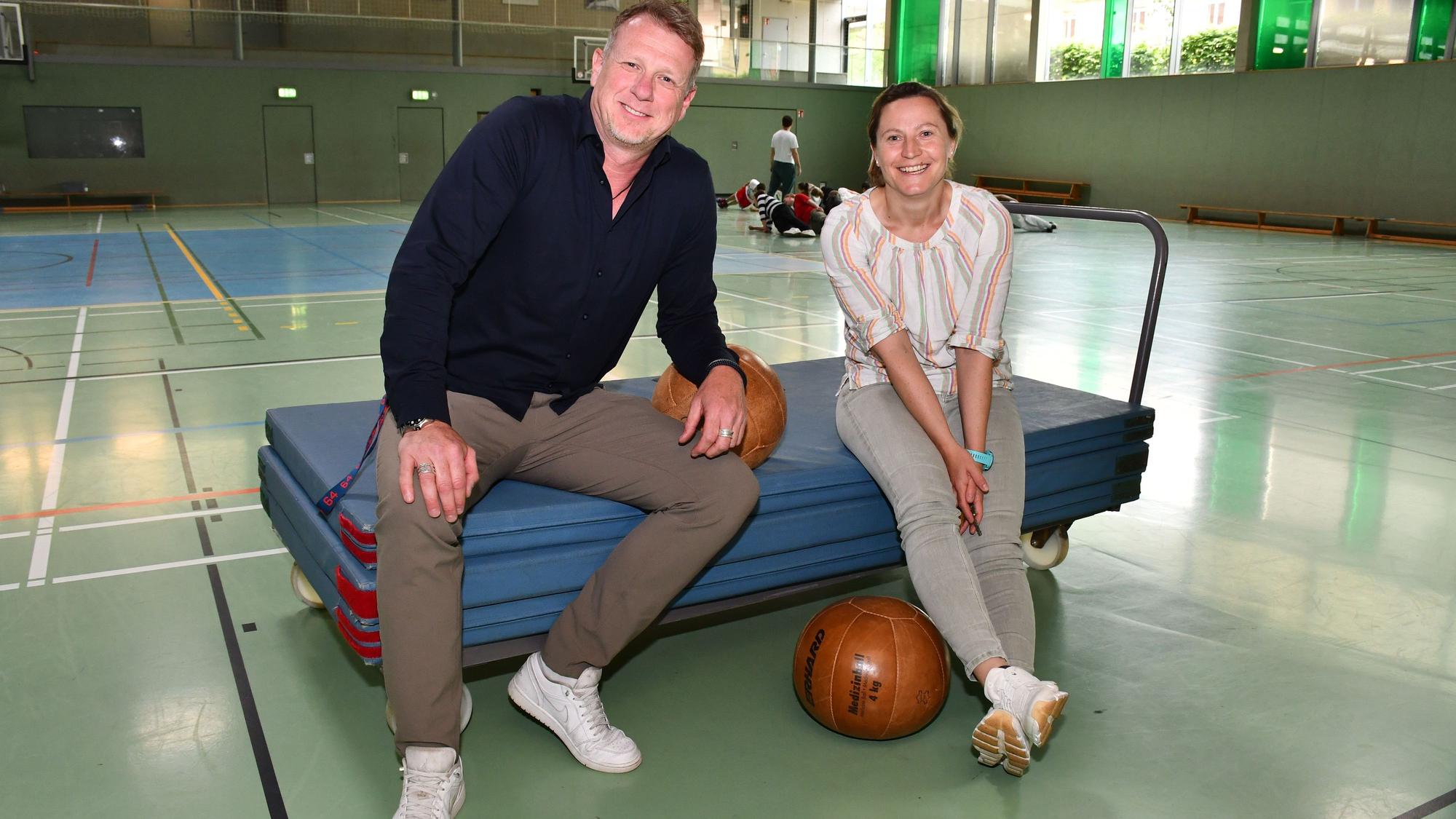 Sportlehrerin Diane Franzky und Schulleiter Carsten Balvin sitzen in der Sporthalle der Friedrich-Ebert-Realschule auf einem Mattenwagen.