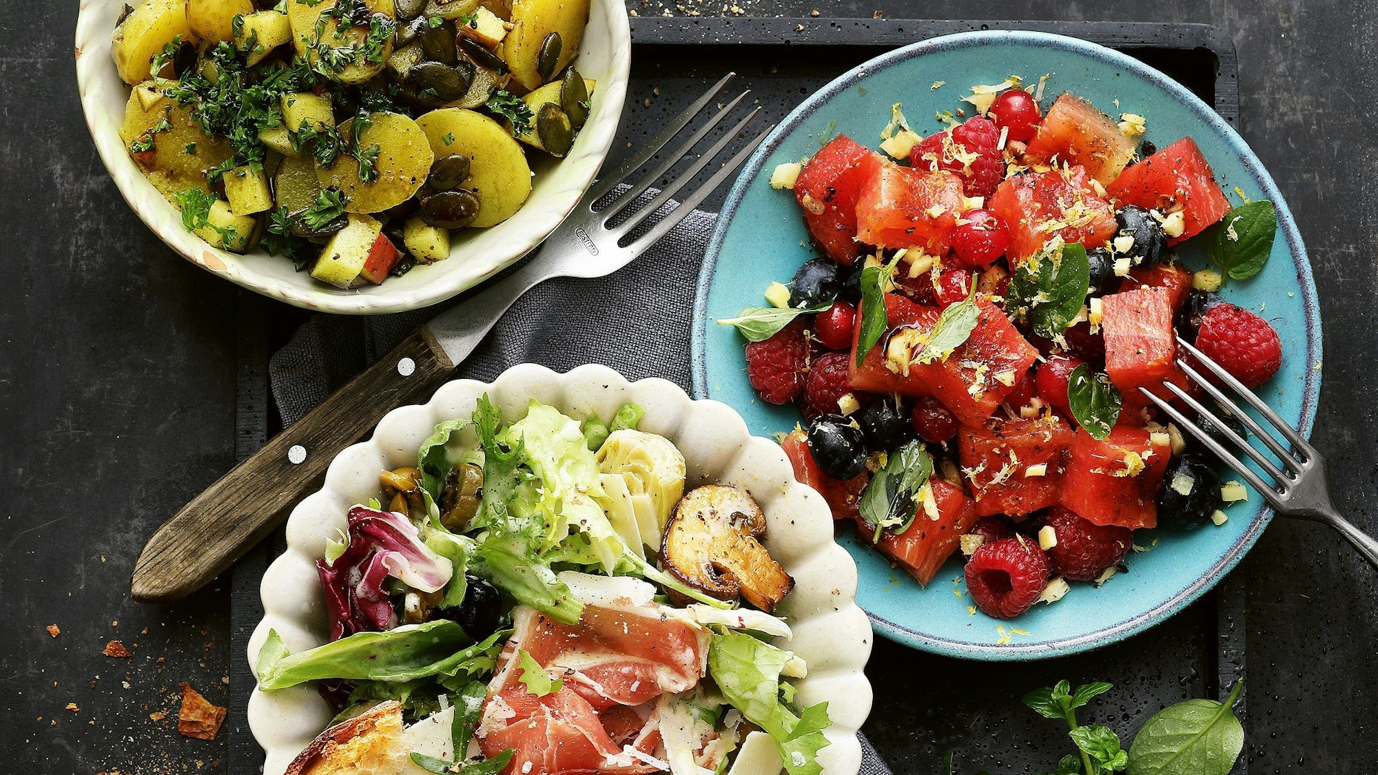 drei verschiedene Salate in Schalen und auf einem Teller