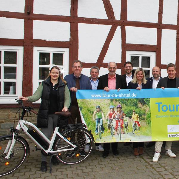 Die Vertreter der beteiligten Kreise und Kommunen halten vor einem Fachwerkgebäude in Antweiler ein Banner, mit dem für die „Tour de Ahrtal“ geworben wird.