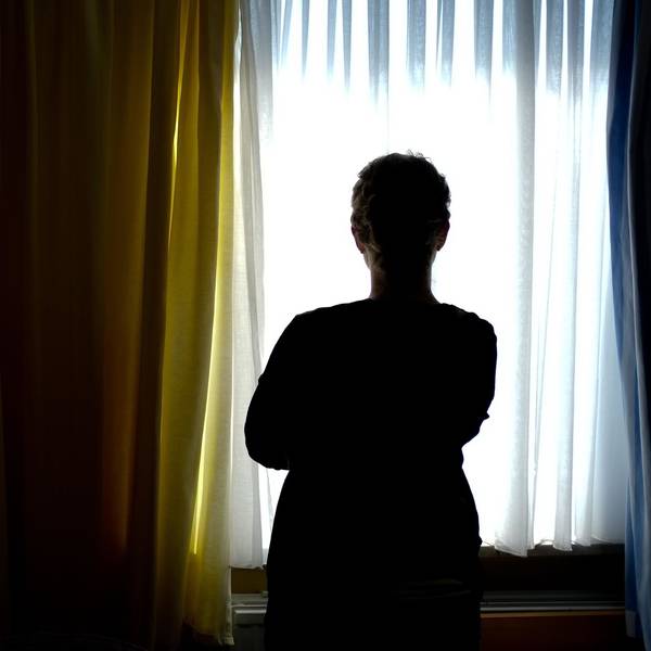 Eine Person steht vor einem Fenster und ist im Gegenlicht nur als dunkle Silhouette erkennbar.