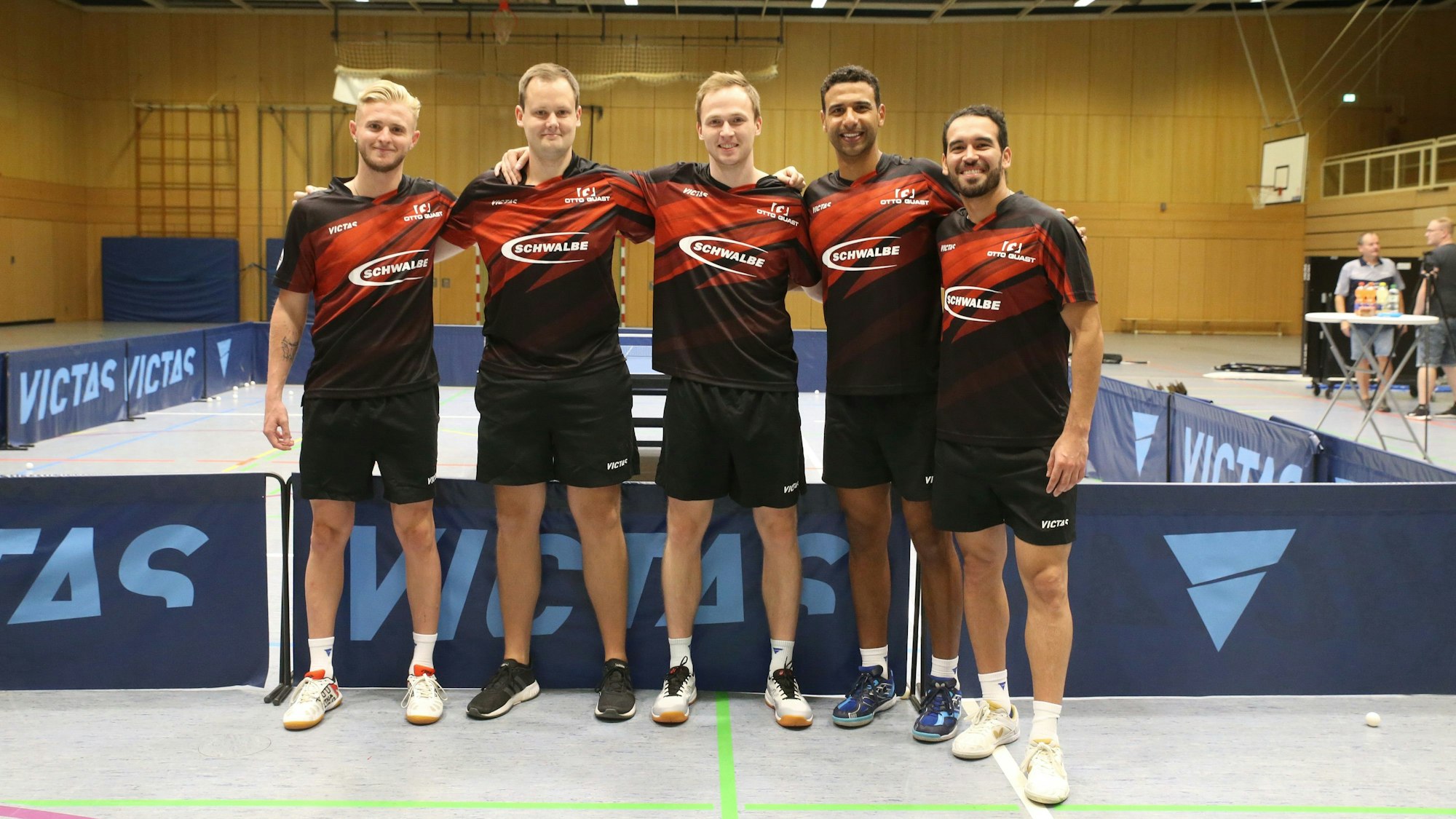 Vier Tischtennisspieler und ihr Trainer stehen Arm in Arm in einer Reihe.