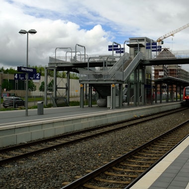 Der Blick auf die Fußgängerbrücke im Mechernicher Bahnhof, in dem ein Regionalzug hält.