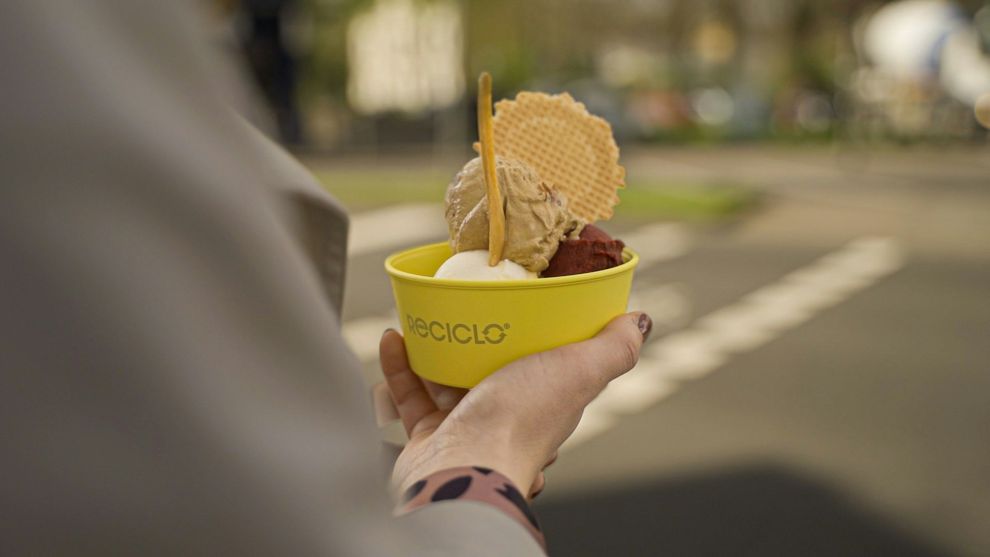 Das Foto zeigt einen gelben Eisbecher, den eine Frau in ihrer Hand hält.