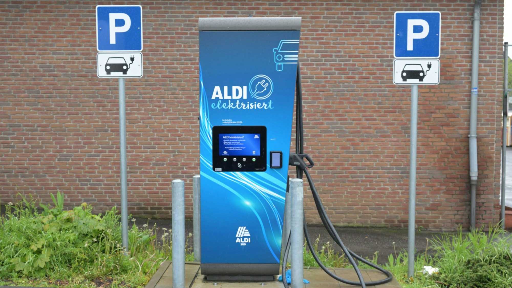 Eine E-Ladesäule mit der Aufschrift „Aldi“ steht vor einer Mauer.