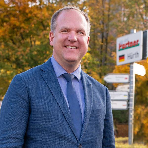 Das Foto zeigt Dirk Breuer vor einem Schilderbaum mit den Namen der Partnerstädte.
