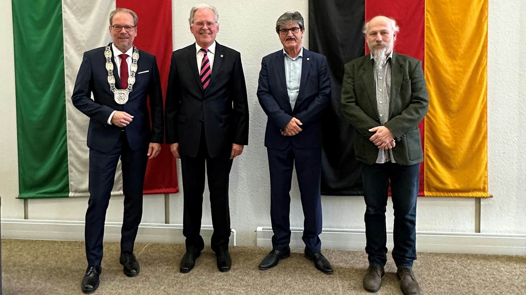 Das Foto zeigt Bürgermeister Volker Mießeler und die neuen Bergheimer Ehrenbürger Johannes Hübner, Helmut Paul und Peter Hirseler. Sie stehen vor den Flaggen von NRW und Deutschland.