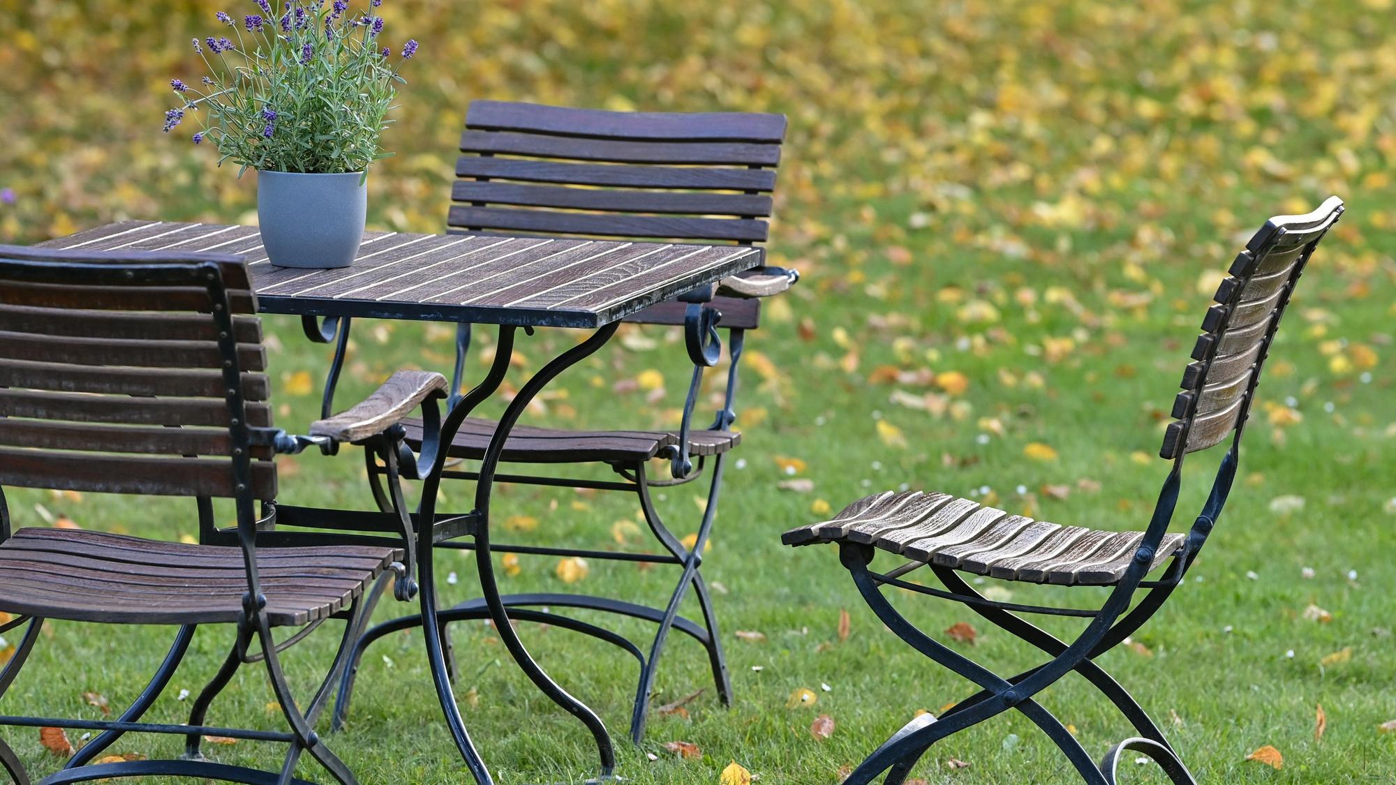Gartenmöbel stehen auf einer Wiese mit bunten Herbstlaub.