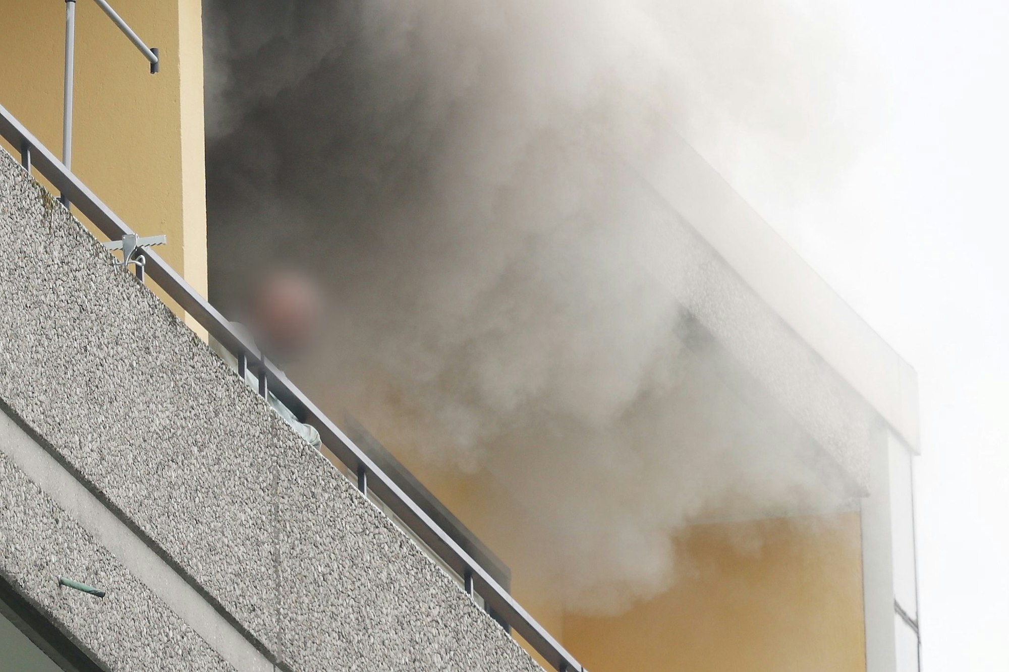 Ratingen: Eine Person steht auf dem Balkon von einem Hochhaus, aus dem Rauch quillt.
