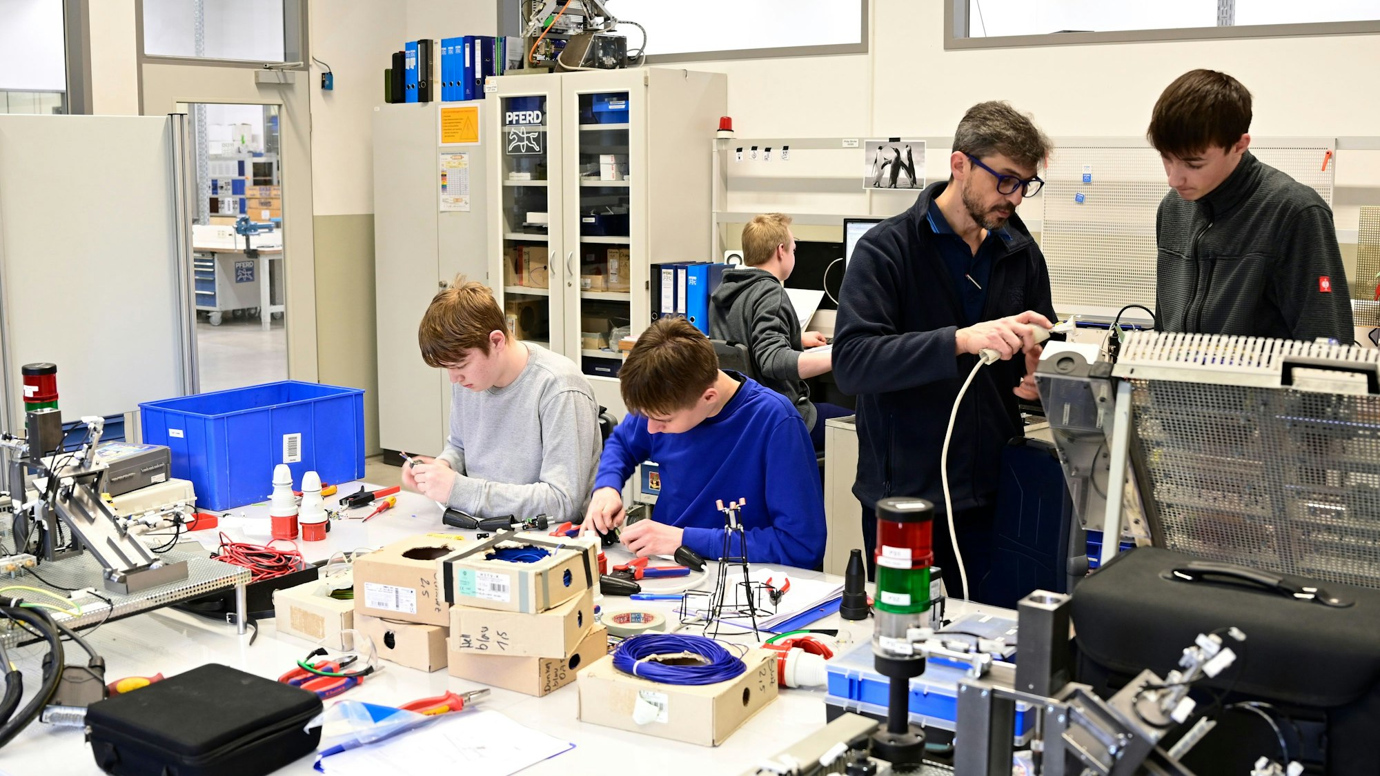 Auszubildende arbeiten in einer Werkstatt. Ein Ausbildungsleiter erklärt das Vorgehen.