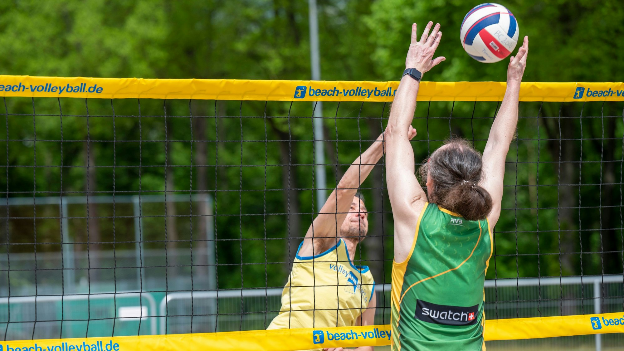 Zwei Beachvolleyballer spielen einen Ball über das Netz.