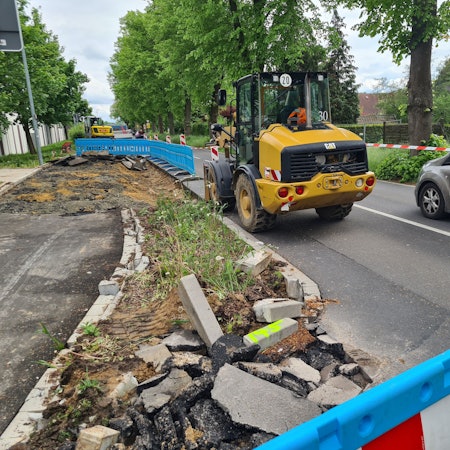 Die Bushaltestelle an der Dansweilerstraße in Glessen wird dargestellt. Ein Baufahrzeug und ein Auto sind vordergründig an einer abgesperrten Baustelle zu sehen.
