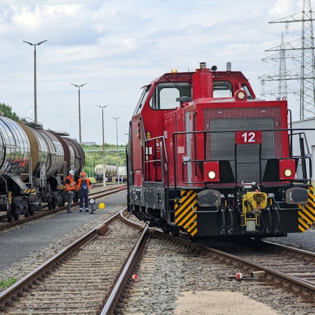 Der Chemiepark Knapsack in Hürth. Zwischen Gleisen und zwei Zügen stehen zwei Gleisarbeiter in orangenen Westen mit Bauhelmen.