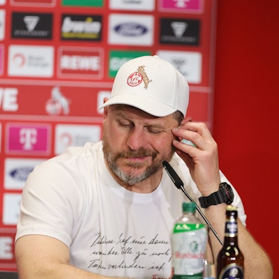 Steffen Baumgart, Trainer des 1. FC Köln, bei einer Pressekonferenz am Geißbockheim. Baumgart sitzt vor einem Mikrofon, im Hintergrund ist eine Wand mit Sponsoren zu sehen.