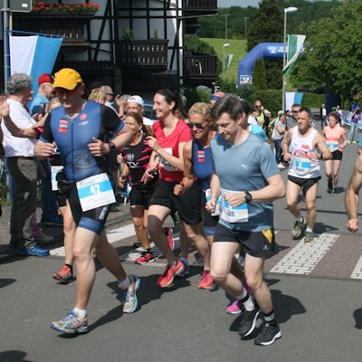 Der Biesfelder Dorflauf 2019. Mehrere Läufer und Läuferinnen in Sportklamotten sind zu sehen. Publikum feuert die Athleten und Athletinnen an.
