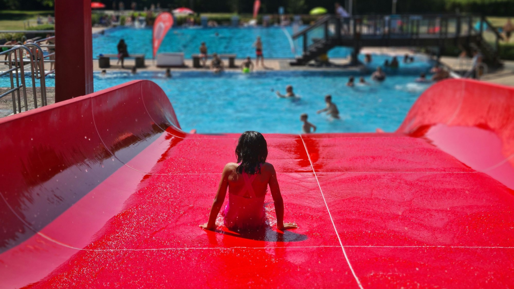 Auf dem Foto ist ein Mädchen zu sehen, das in Freibad Bedburg eine rote Rutsche herunterrutscht.