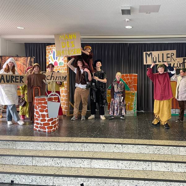 Theateraufführung bei der Feier 50 Jahre Gutenbergschule. Kinderschauspieler und Kinderschauspielerinnen halten Schilder hoch und schauen in die Kamera.