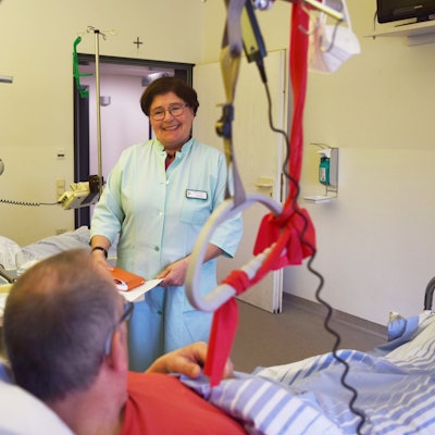 Marianne Kesseler steht in einem grünen Kittel am Bett eines Patienten in einem Zwei-Bett-Zimmer der Unfallstation im Kreiskrankenhaus Mechernich.