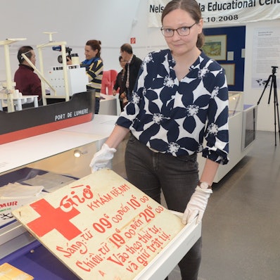 Das Schild, das die Öffnungszeiten der Krankenstation nannte, wird von Kuratorin Bernadette Fischer gezeigt.