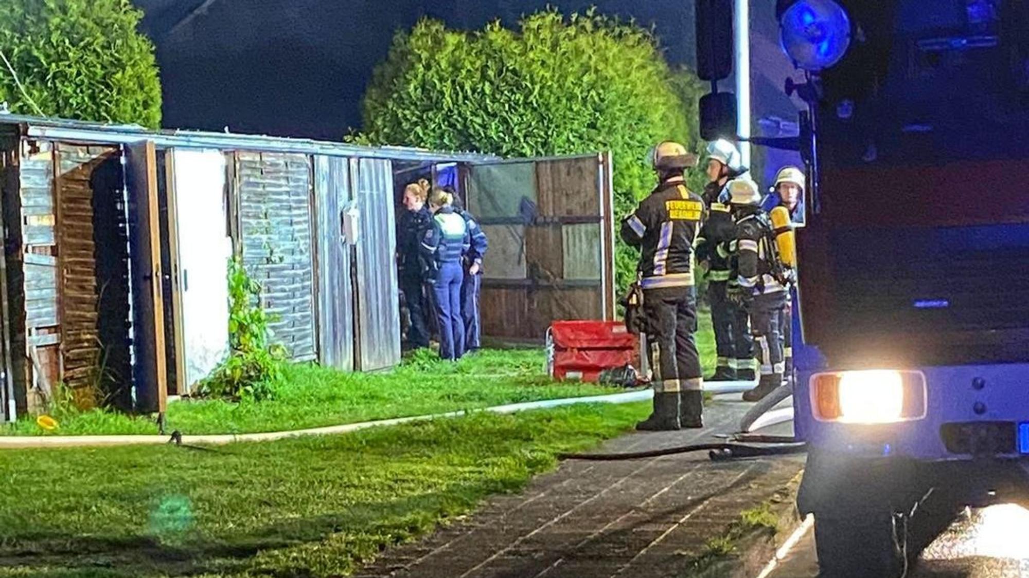 Das Foto zeigt Feuerwehrleute und Polizisten, die die Laube begutachten, nachdem das Feuer gelöscht worden war.