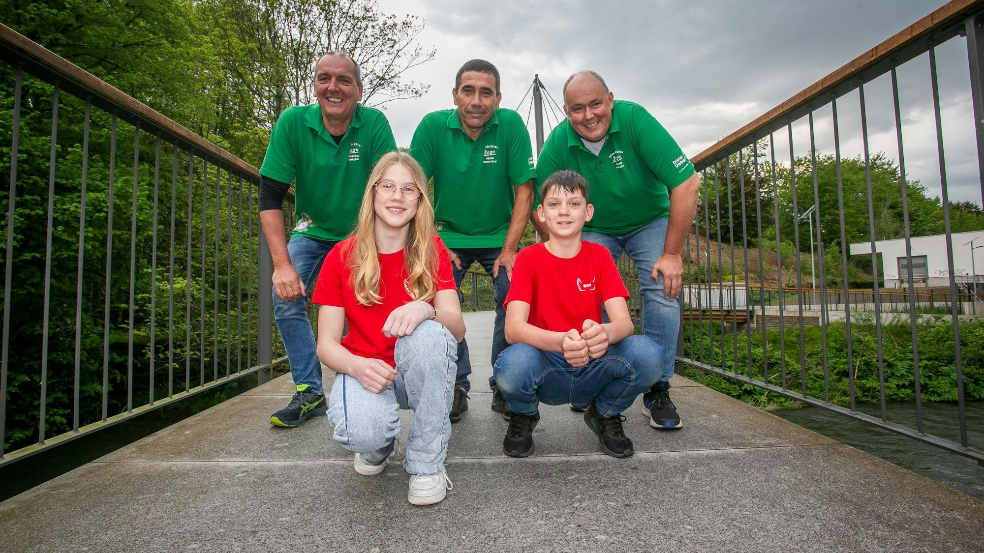 Drei Männer sowie ein Mädchen und ein Junge stehen gemeinsam für ein Gruppenbild. Die Kinder knien vor den Erwachsenen in einer vorderen Reihe.
