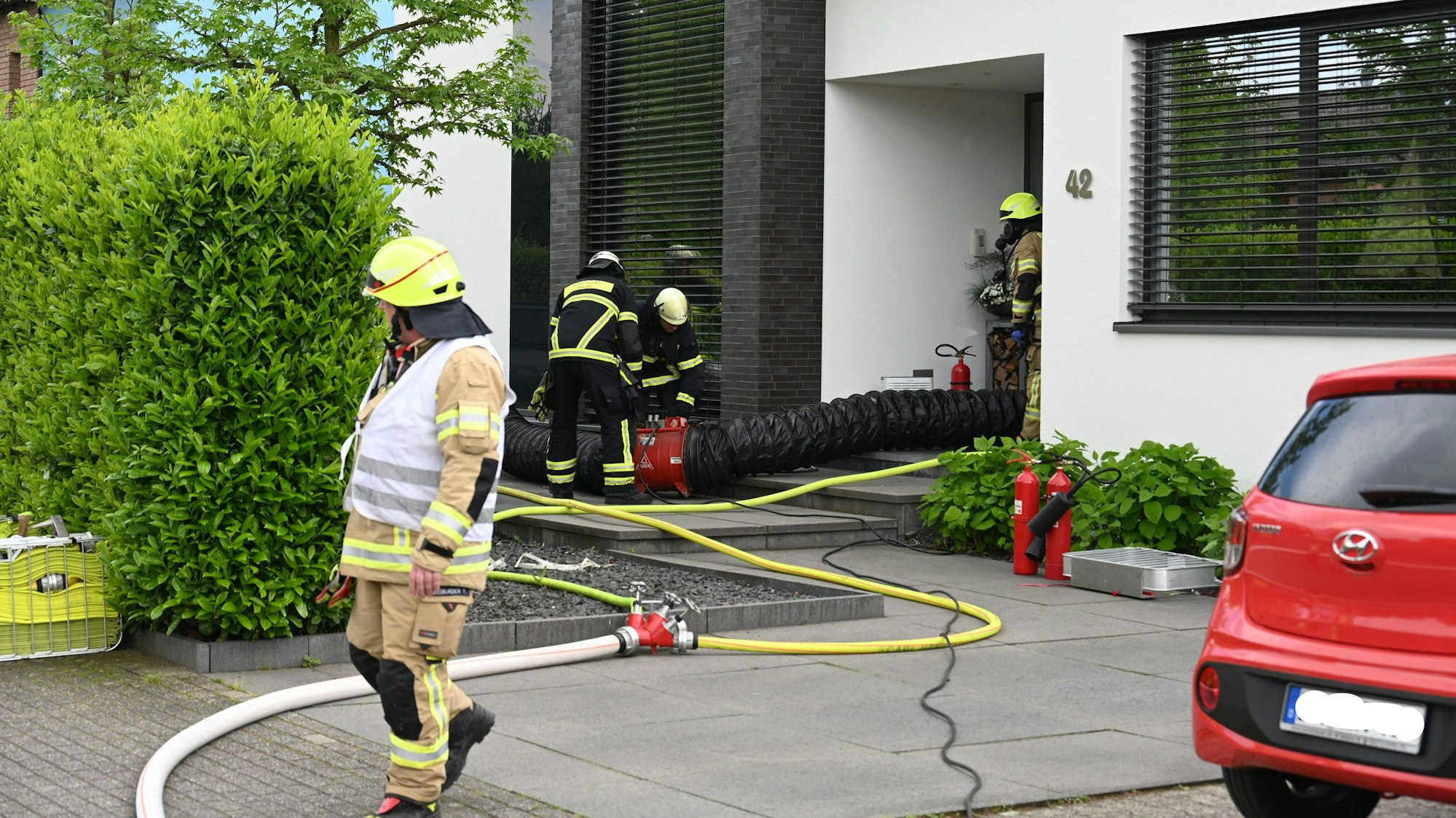 Feuerwehrleute laufen vor einem Hauseingang. In das Haus hinein führt ein Schlauch.