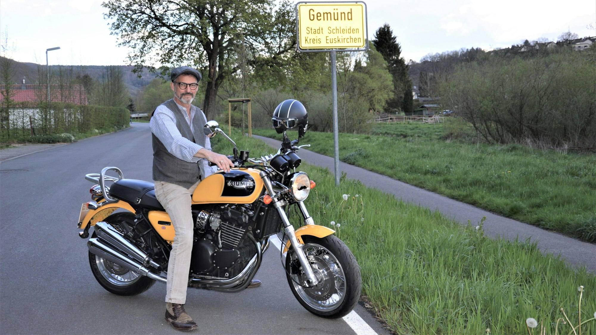 Wolfgang Meyer aus Gemünd sitzt vor dem Ortsschild Gemünd auf seinem Motorrad und schaut in Richtung Kamera.