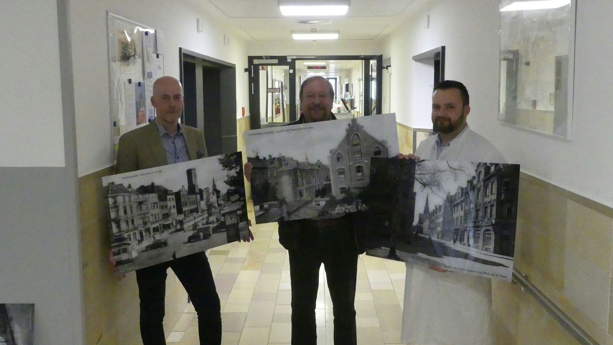 Josef Valenthorn, Geschäftsführer, Josef Wirges, Vorsitzender des Fördervereins und Adam Frey, Abteilungsleiter im St. Franziskus-Hospital, zeigen Bilder mit historischen Motiven von Köln und Ehrenfeld.
