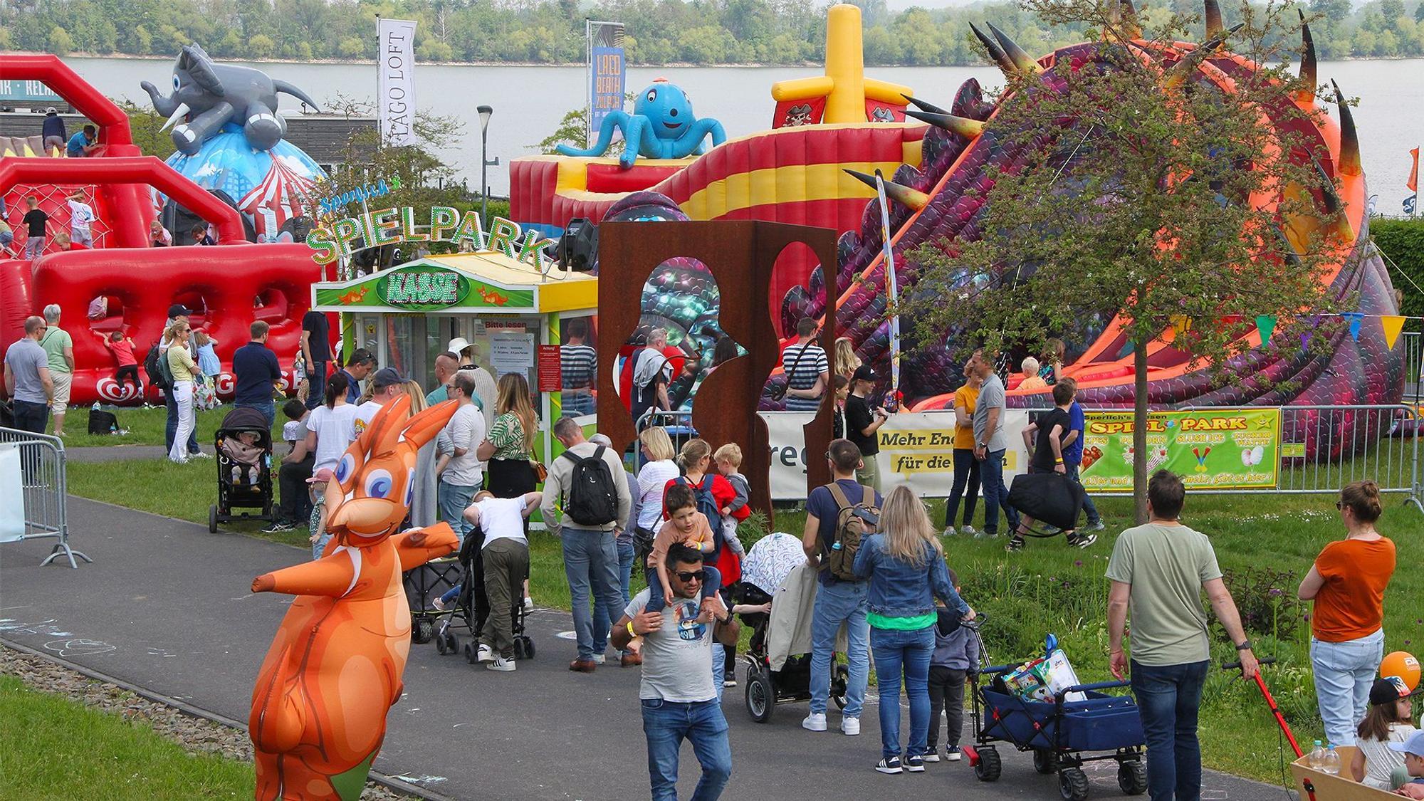 „Jump im Park“ in Zülpich ist ein Hüpfburgenfestival. Vor einer Vielzahl an verschiedenen Hüpfburgen sind junge wie erwachsene Besucher und Besucherinnen zu sehen.
