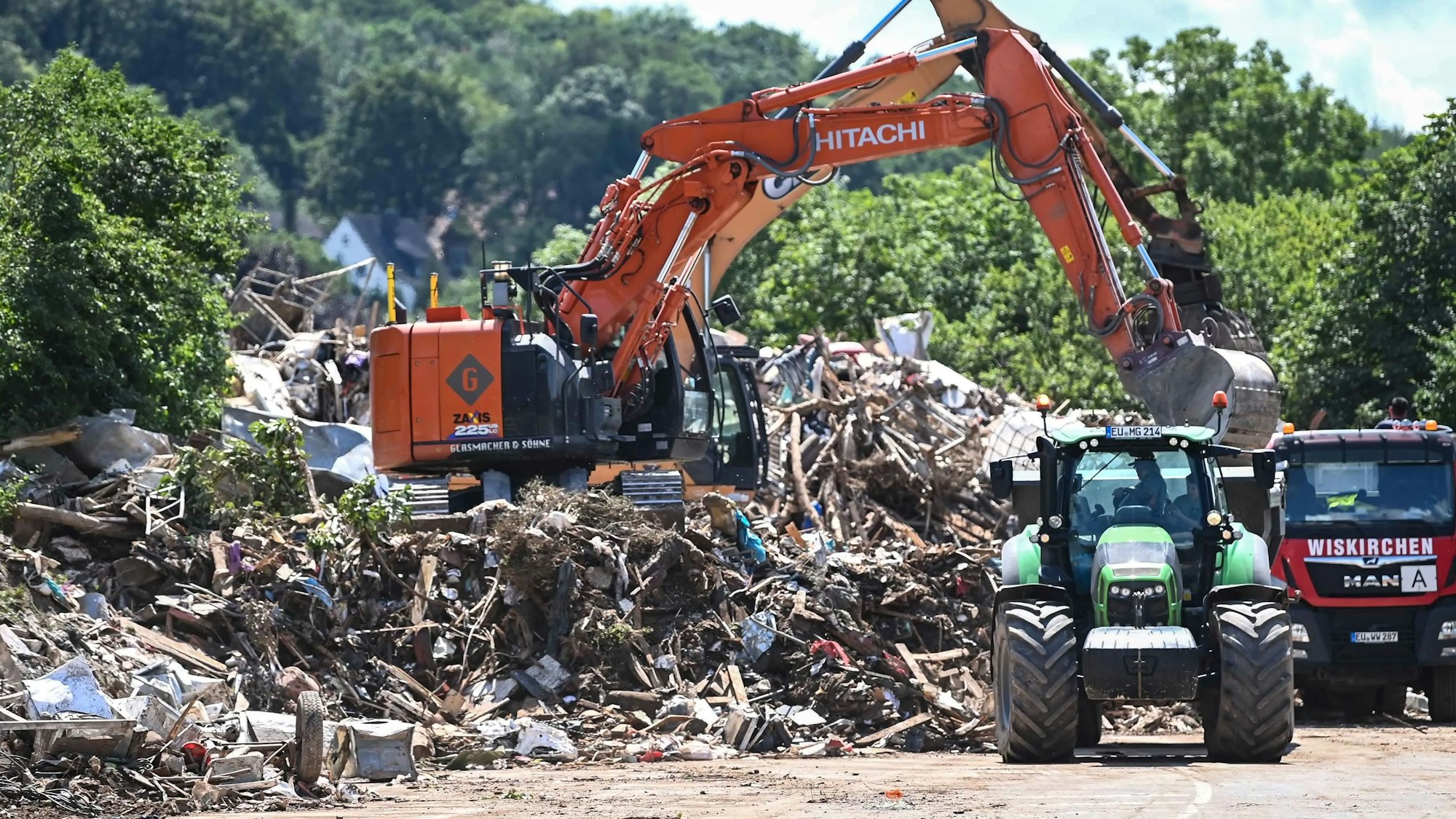 Ein Bagger steht auf einem Müllberg und lädt Sperrmüll in einen Lkw und einen Traktor.