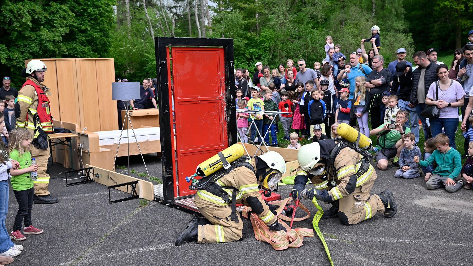 Feuerwehrleute montieren einen Feuerwehrschlauch. Im Hintergrund beobachten Zuschauer die Szenerie.