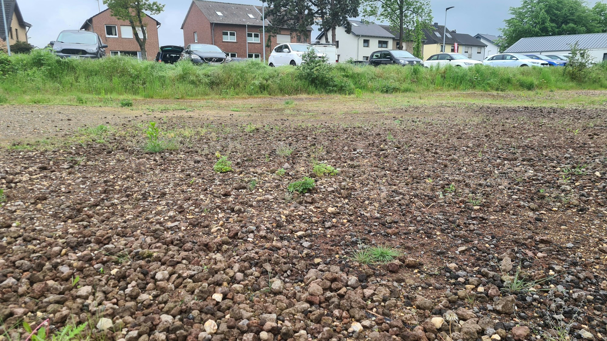 Die Fläche des alten Sportplatzes in Lipp. Es ist eine Schotterfläche zu sehen, im Hintergrund parken Autos und stehen Häuser.