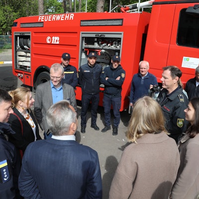 Feuerwehrleute und Zivilisten stehen in einem Kreis vor einem Tanklöschfahrzeug.