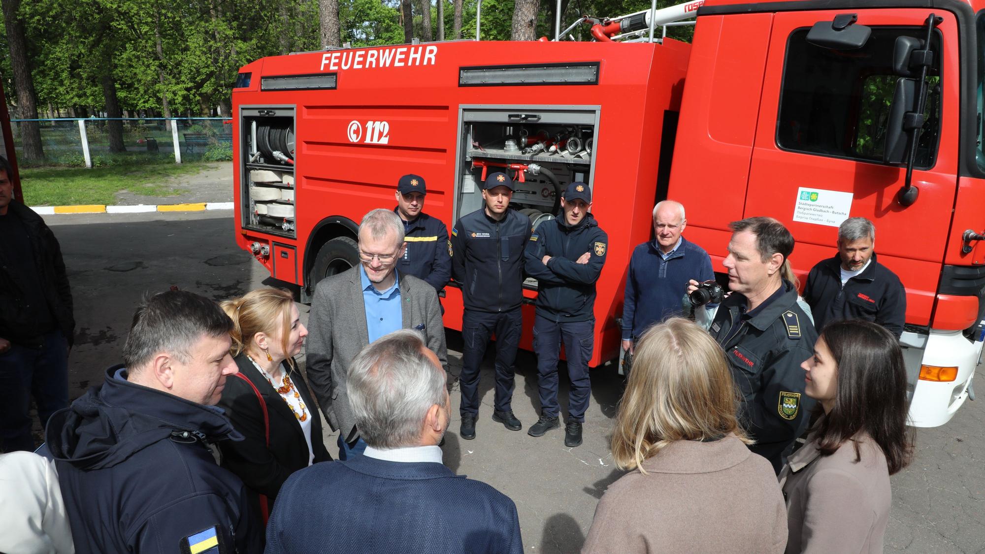 Feuerwehrleute und Zivilisten stehen in einem Kreis vor einem Tanklöschfahrzeug.