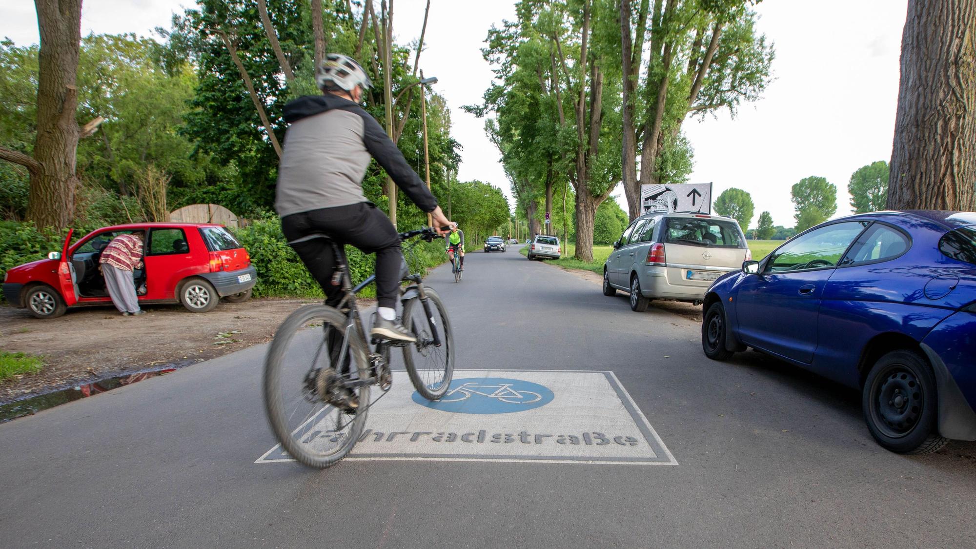 Ein Radfahrer fährt über das Piktogramm Fahrradstraße, das auf eine schmale Straße aufgebracht wurde.