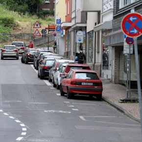 Links auf dem Foto sind Radfahrer auf dem Radstreifen unterwegs. Auf dem Parkstreifen rechts im Bild parken Autos. Auf der Fahrbahn in der Mitte fahren Autos.